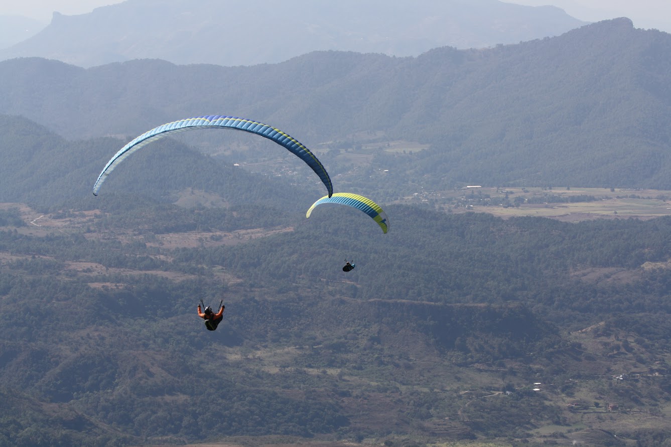 Two paragliders soaring cross-country over Valle de Bravo terrain